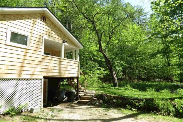 Side yard view of the Vermont cottage showing the driveway area, stone wall, and the lower section of the property near the house.
