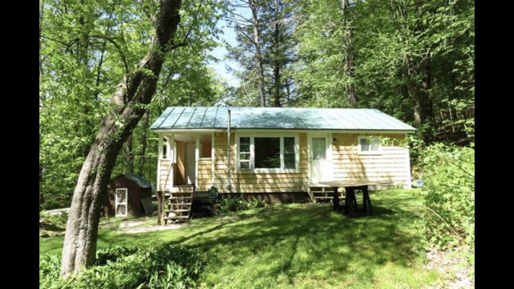 Front exterior of the Vermont cottage on closing day with the original yard and wooded hillside surrounding the house.